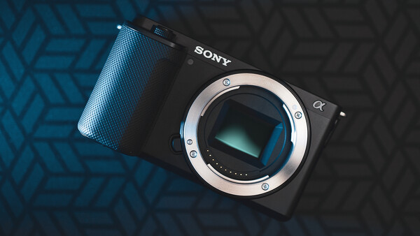 Sony mirrorless camera body with lens mount exposed, positioned on blue and black geometric patterned surface.
