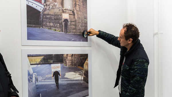 Man pointing at framed photograph on gallery wall during exhibition.