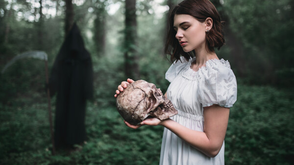 Woman in white period dress holding a mushroom in a dark forest clearing.