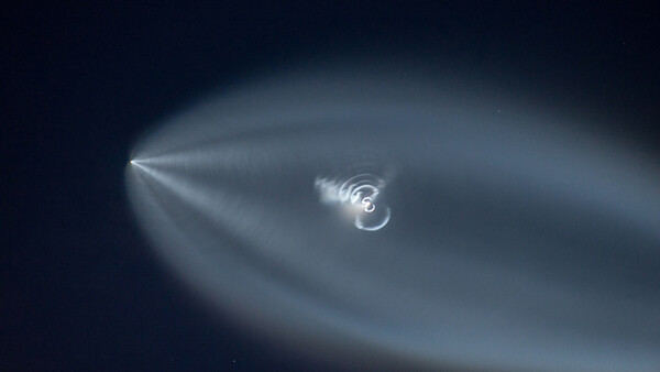 Spiraling blue-white light phenomenon against dark night sky with radiating streaks.