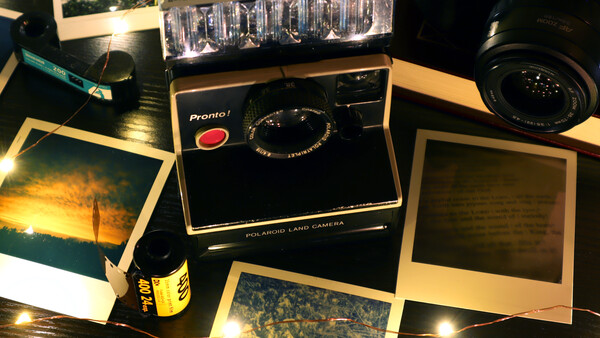 Vintage Polaroid Pronto I instant camera surrounded by Polaroid prints and photography equipment on a dark surface.