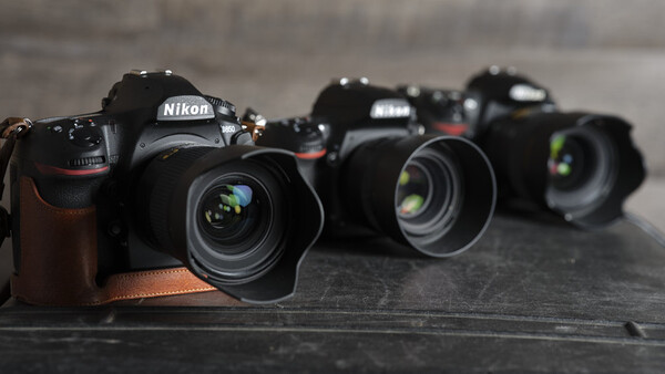 Three Nikon DSLR cameras with attached lenses arranged in a row on a dark surface.