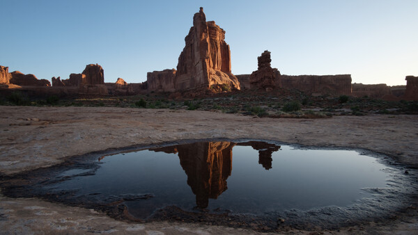 Desert rock formations reflected in a still pool of water at golden hour.