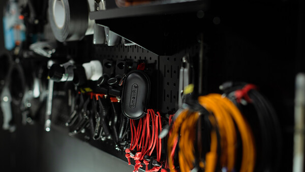 Close-up of a pegboard wall organizer with red and yellow coiled cables and black mounted tools against dark background.