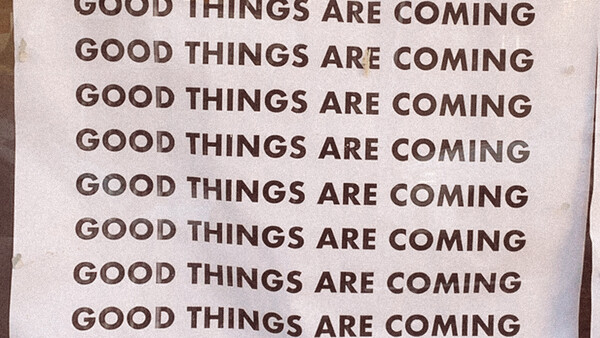 Repeated text reading "GOOD THINGS ARE COMING" printed in brown typography on a light background.