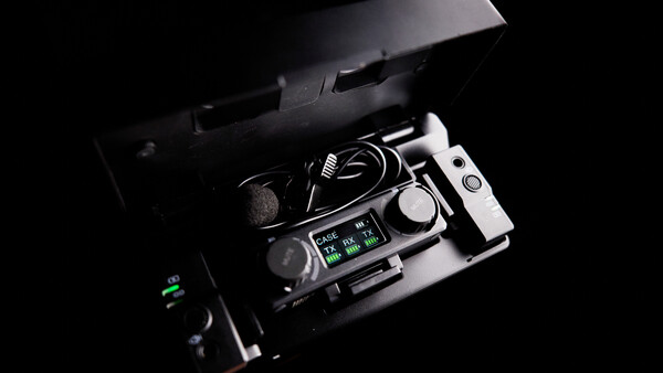 Professional audio recorder with microphone and cables displayed in an open carrying case against black background.