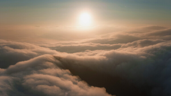 Sun rising above a thick blanket of clouds with dramatic golden light illuminating the cloud formations.