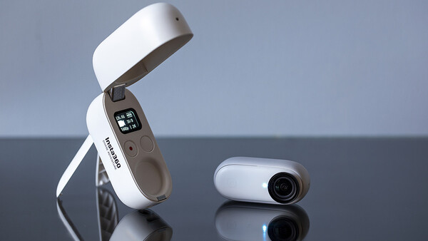 Two compact white and gray devices displayed on a reflective surface against a blue-gray background.