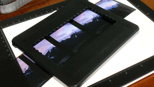 Film strip contact sheet displayed on a black light table alongside rulers and photographic prints.
