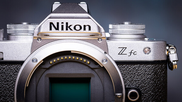 Nikon Zfc mirrorless camera body displayed front-on with lens mount visible and two lenses positioned beside it.