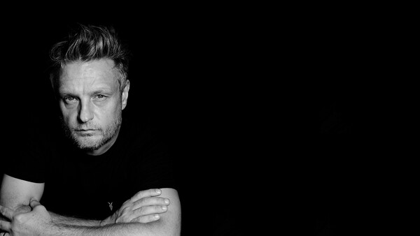 Black and white portrait of a man with styled hair against a dark background.
