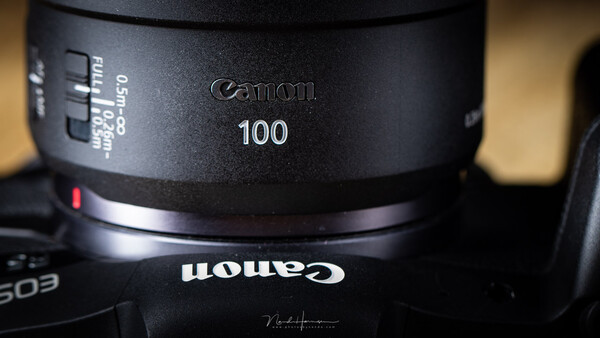 Canon 100mm telephoto lens barrel with focus ring and distance markings visible.
