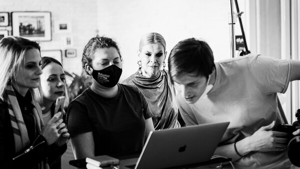 Five people gathered around a laptop screen in a bright studio space, examining content together.