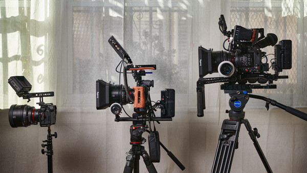 Three cinema cameras mounted on tripods with microphones and support rigs in a studio setting.
