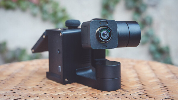 Black motorized gimbal with compact camera mounted on woven surface outdoors.