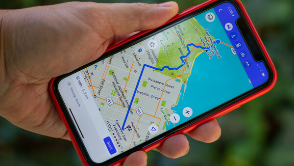 Screenshot of a navigation app displayed on a red smartphone held in someone's hand outdoors.