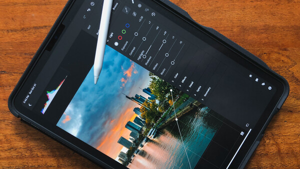 iPad displaying a landscape photo with editing interface and Apple Pencil resting on screen.
