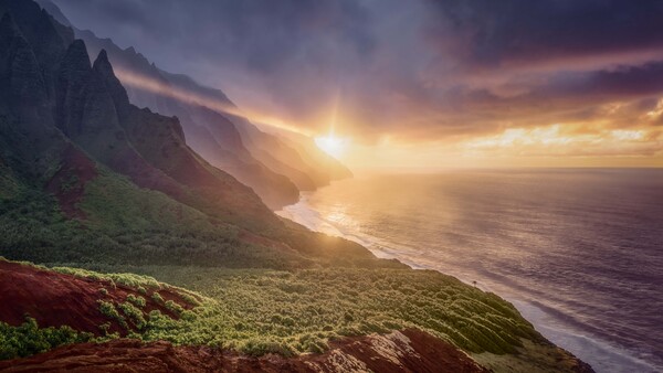 Dramatic coastal landscape with steep green cliffs overlooking a beach and ocean at golden hour sunrise or sunset.