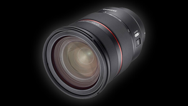 Professional camera lens with red accent ring, displayed against black background with dramatic lighting.