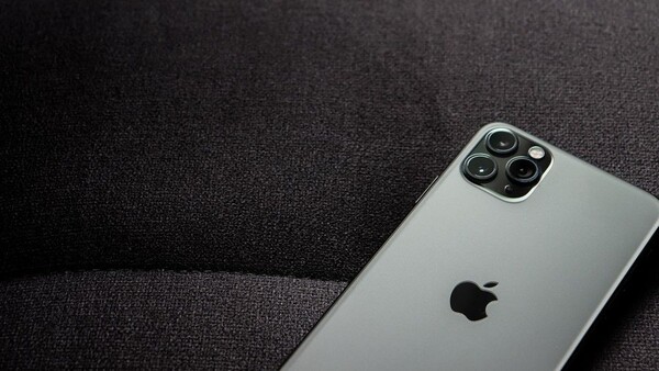 Silver iPhone with quad camera system positioned on dark textured fabric surface.