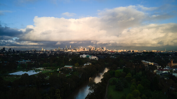 City skyline with river in foreground under dramatic cloudy sky at golden hour.