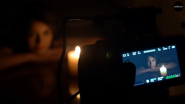Mobile phone recording video in low-light setting with warm ambient lighting and a monitor displaying the live feed.