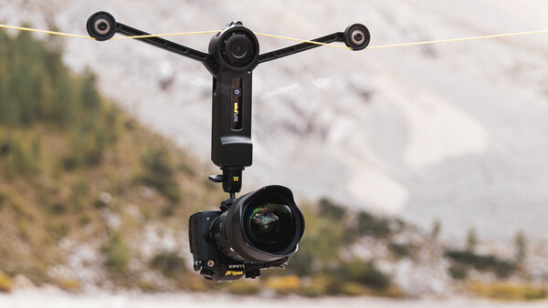 Gimbal-mounted camera rig suspended in air with mountainous landscape below.