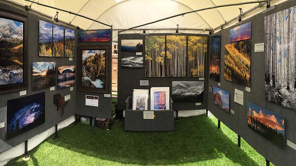 Photography exhibition tent with landscape images displayed on dark panels and central pedestals.