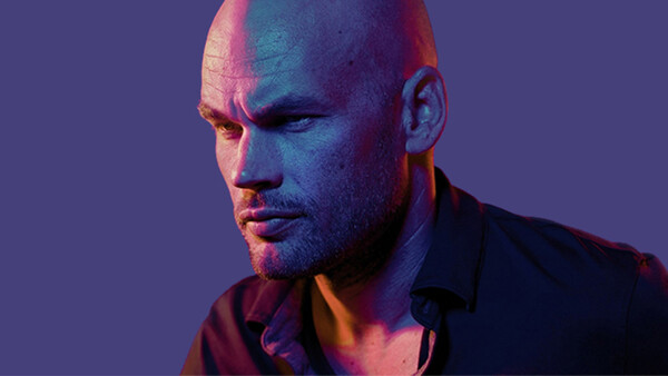 Bald man with facial hair against purple background with warm and cool lighting.