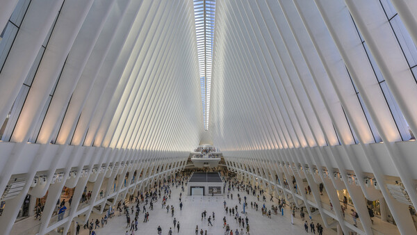 Interior of the Oculus transit hub with symmetrical white ribbed ceiling and crowds of people in the floor-level concourse.
