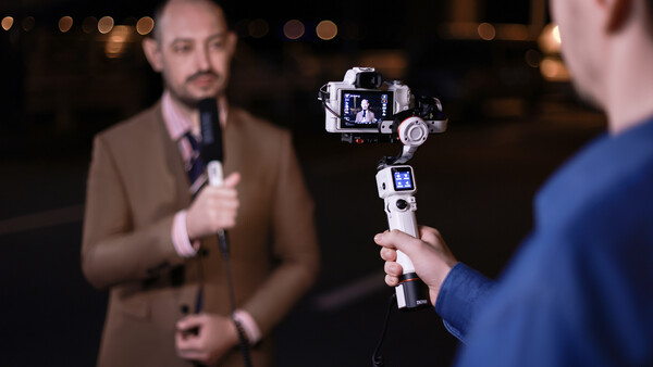 Man holding a smartphone gimbal stabilizer with mounted camera during evening interview.