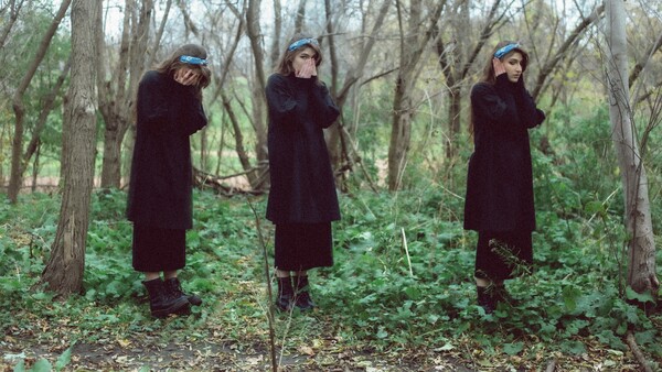 Three people in burgundy coats arranged in a triptych, adjusting their hats in a bare forest.