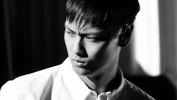 Portrait of a young man in a white shirt, shot in black and white with dramatic side lighting.