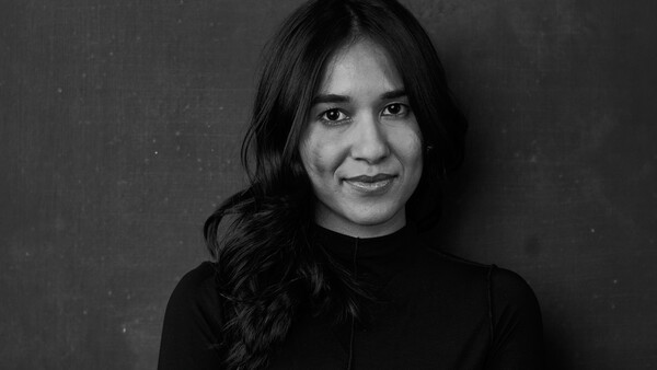 Black and white portrait of a woman with long dark hair wearing a dark turtleneck against a neutral background.