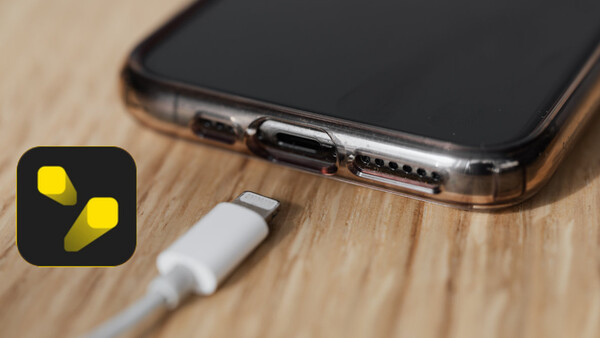 Lightning connector cable plugged into smartphone charging port on wooden surface.
