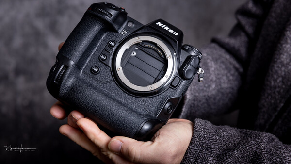 Nikon professional DSLR camera body held in hand, showing the mount and control buttons.