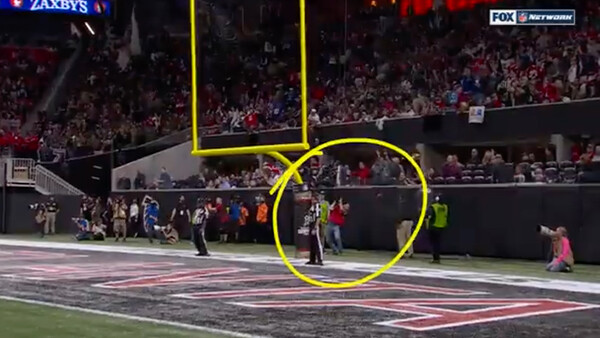 Football stadium field with players and officials during a game, with yellow circle highlighting an area near the sideline.