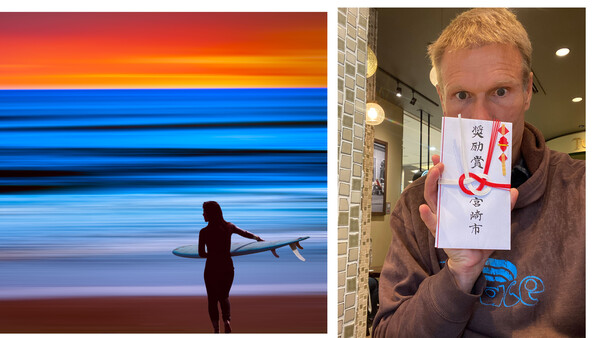 Surfer in wetsuit carrying board at sunset beach with vibrant orange and blue sky.