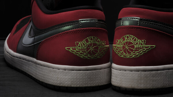Rear view of burgundy and black high-top sneakers with gold winged logo embroidery on heel tabs and white sole.