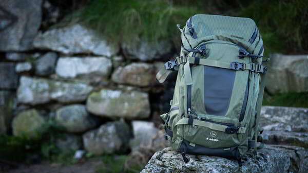 Green hiking backpack sitting on a mossy stone wall with blurred foliage in the background.