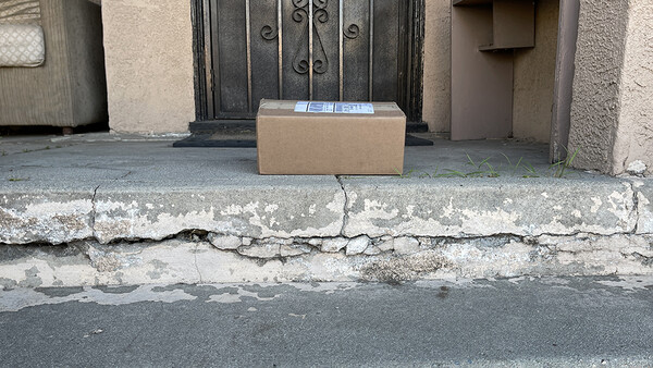 Cardboard delivery box placed on a weathered doorstep with cracked concrete and peeling paint.