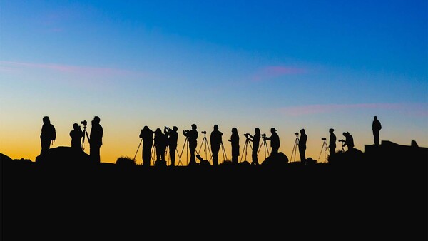 Silhouetted group of people standing on a ridge against a golden and blue sunset sky.