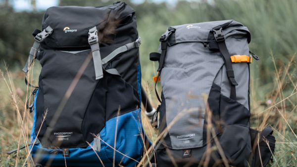 Two hiking backpacks displayed side-by-side in tall grass, one black with blue accents and one gray with orange accents.