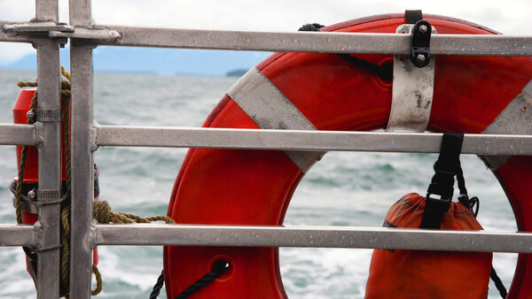 Red and white life preserver rings mounted on gray metal railing with ocean waves visible in background.
