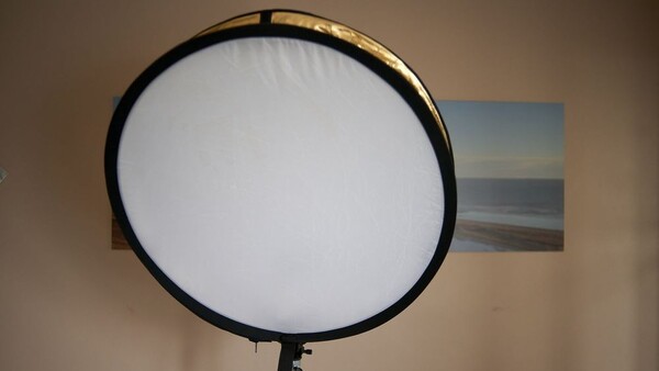 Large circular softbox with diffusion panel mounted on a light stand against a beige wall.
