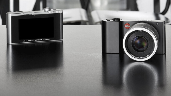 Two Leica digital cameras displayed on a dark surface, shown in profile view with their distinctive designs highlighted.