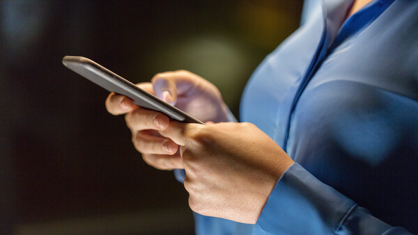 Person in blue shirt holding smartphone with stethoscope visible, shallow depth of field background.