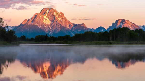 Mountain peak glowing in golden alpenglow light reflected in still water at sunset.