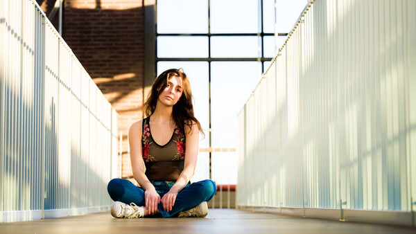 Woman sitting cross-legged in an industrial corridor with metal walls and overhead skylight.