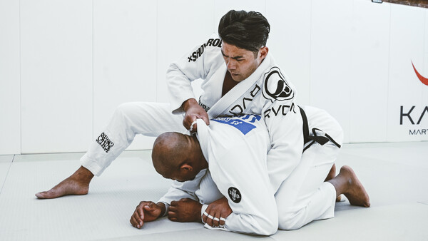 Two martial artists grappling on a white mat during a Brazilian jiu-jitsu training session.
